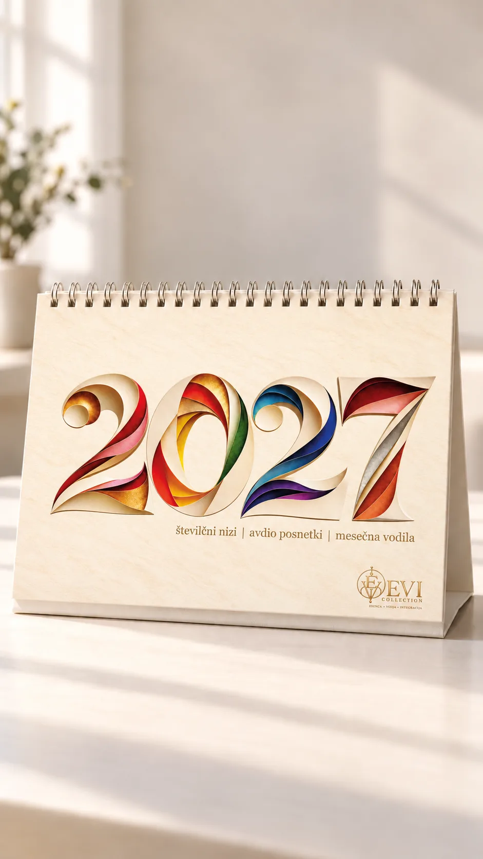 Namizni koledar EVI Collection 2027 z barvito naslovnico na stojalu